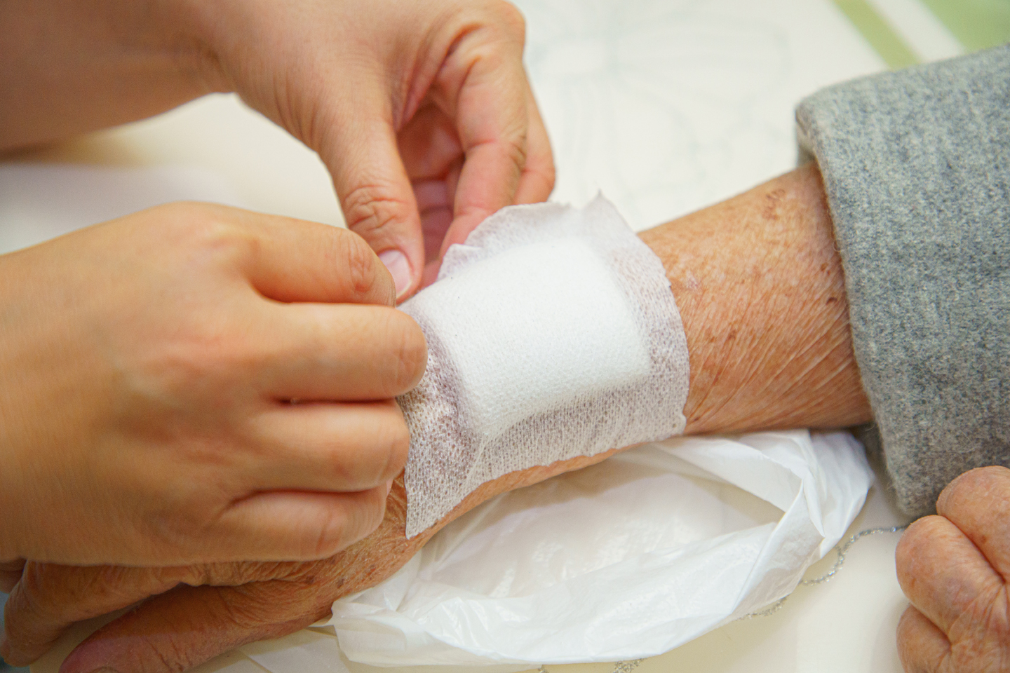 A close-up of someone placing a bandage on the arm of an elderly woman.