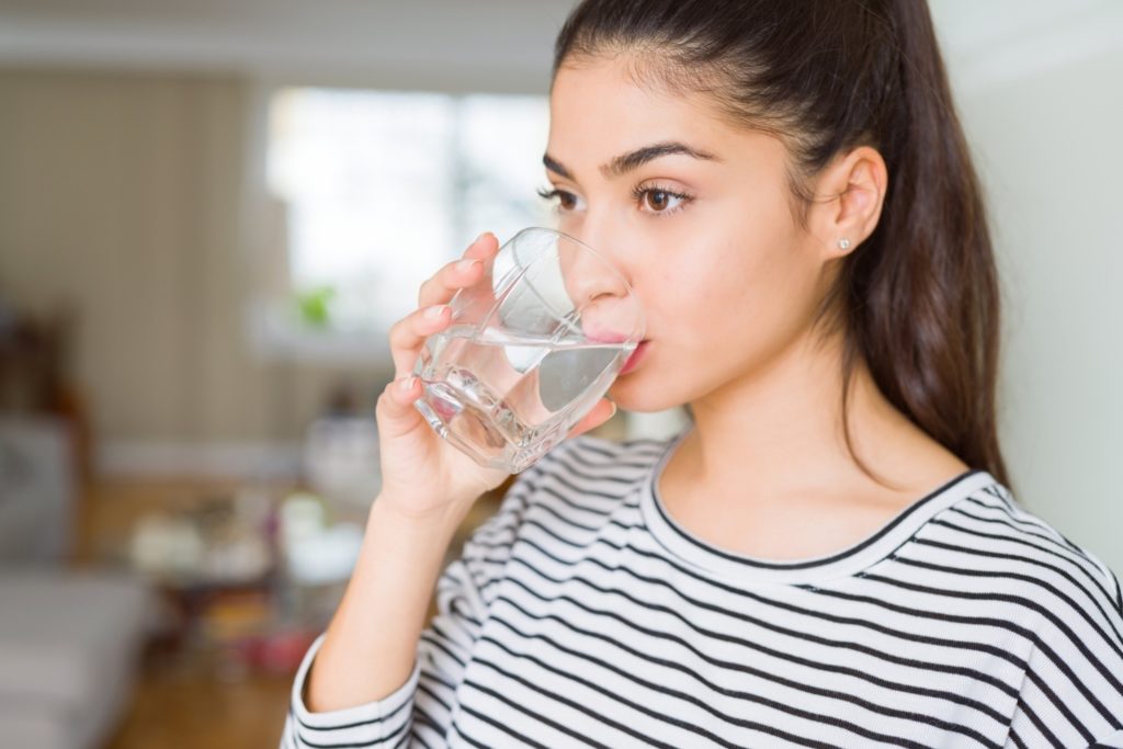A close-up image of a woman in a striped shirt drinking a glass of water.