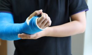 A closeup image of a man with his left hand on his blue right arm cast.
