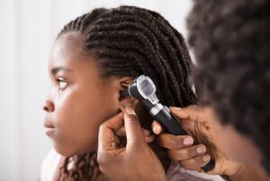 A preteen girl getting her ear examined at the doctor’s office by a female doctor.