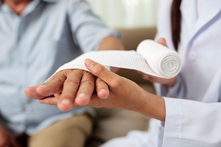 A closeup image of a doctor wrapping a bandage on a male patient’s hand.
