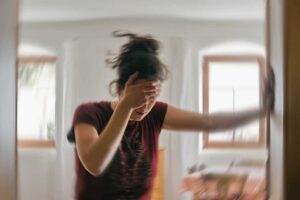 A woman leans against the doorframe with one hand and holds her forehead with the other during a dizzy spell.
