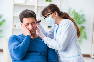 Doctor examines a man’s ear canal as he holds it in pain