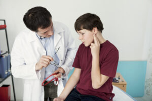 ENT doctor examining young boy's ear with an otoscope while she sits in medical office