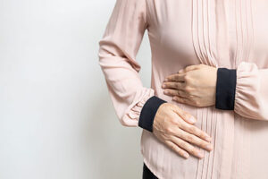 Woman in pink top holding her right abdomen area, indicating abdominal or rib pain