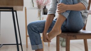 Woman sitting at desk massaging her toe after removing shoe due to discomfort and pain.