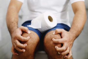 Person holding toilet paper roll while seated on toilet.