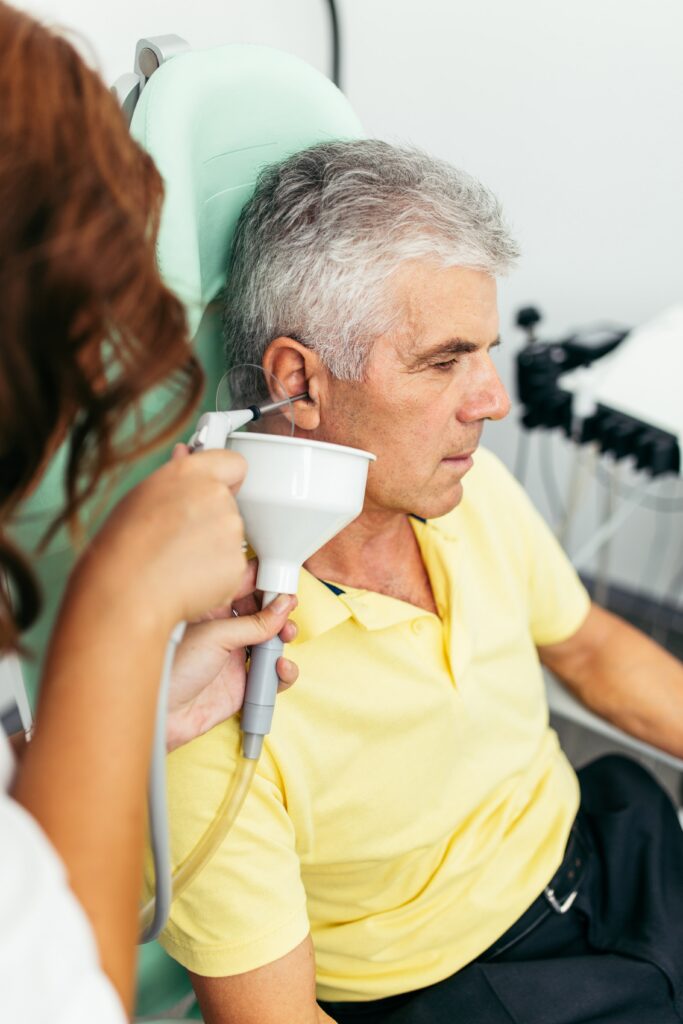 Healthcare professional examines senior man's ear using medical instrument during clinical examination