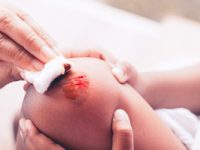 Parent helping her child perform first aid knee injury after she has been an accident