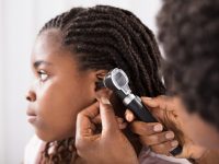 A preteen girl getting her ear examined at the doctor’s office by a female doctor.